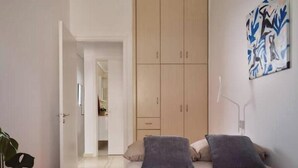 Een slaapkamer met een bed, een kledingkast, een plant en een schilderij aan de muur.
