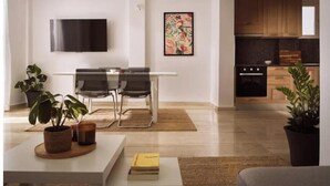 Een moderne woonkamer met een flatscreen televisie, een eethoek met stoelen, een keuken met houten kasten en potplanten.