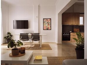 Ein modernes Wohnzimmer mit Flachbildfernseher, einem Essbereich mit Stühlen, einer Küche mit Holzschränken und Topfpflanzen.