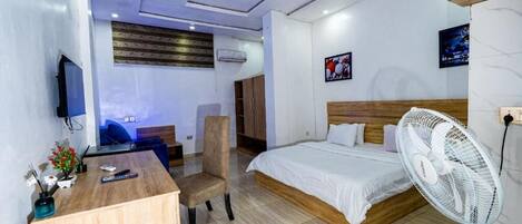 Une chambre d’hôtel équipée d’un lit, d’un bureau, d’une chaise, d’une télévision et d’un ventilateur.