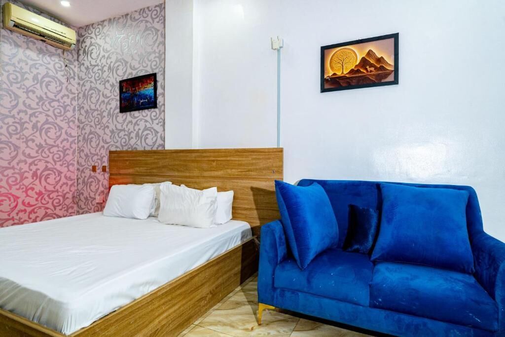 A bedroom with a wooden bed, white bedding, a blue sofa, patterned wallpaper, and a framed picture on the wall.