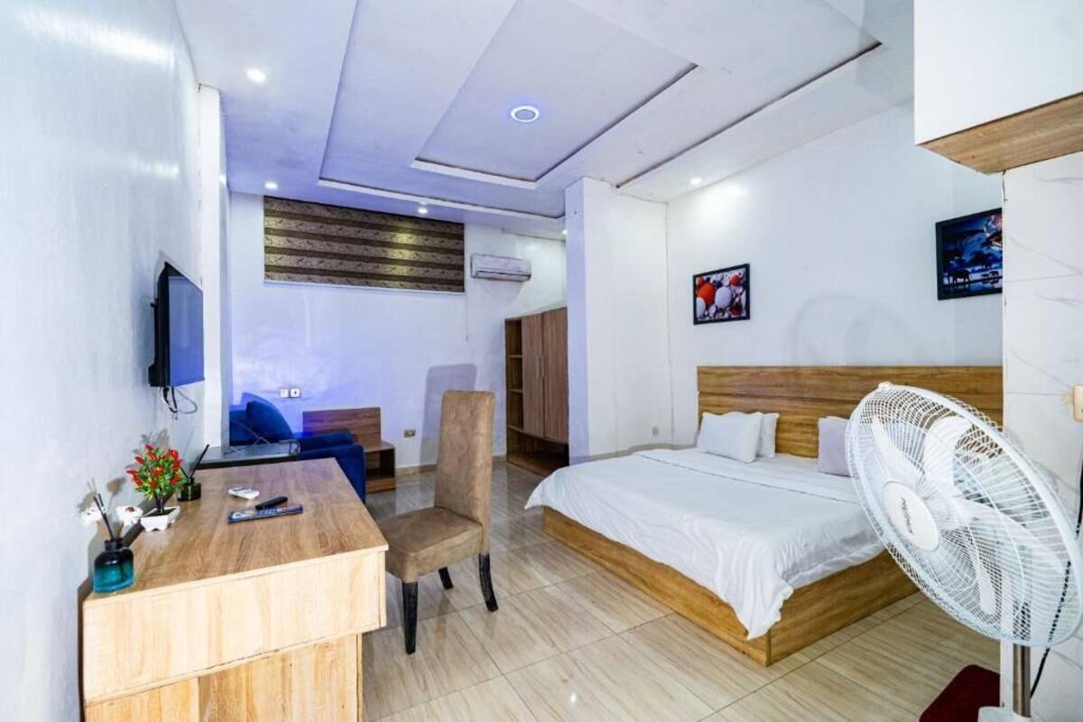 Una habitación de hotel con cama, escritorio, silla, televisor y ventilador.