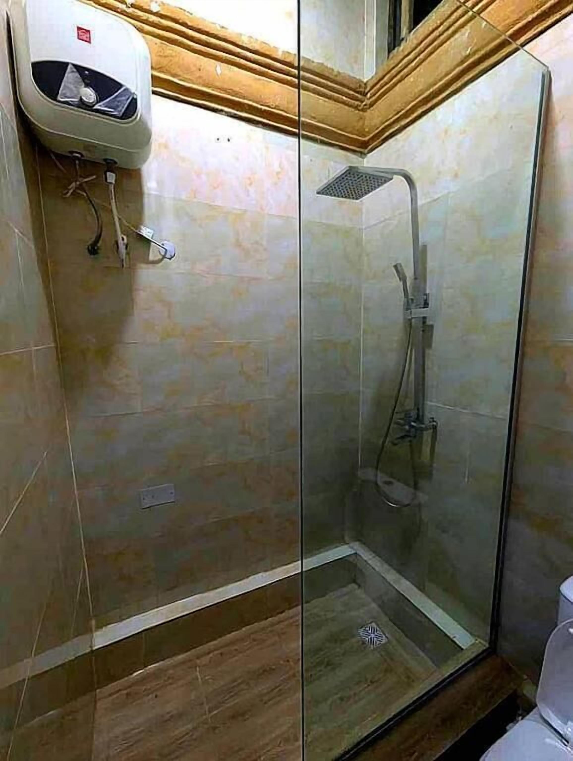 A shower area with a glass enclosure, a handheld showerhead, and a wall-mounted heater.