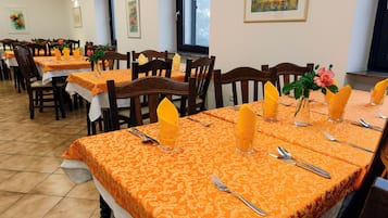Ein Essbereich mit vier gedeckten Tischen, Holzsesseln und orangefarbenen Tischdecken.