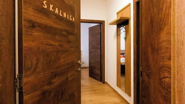 A wooden door with 'SKALNICA' carved on it, leading to a hallway with a wooden floor and a mirror on the wall.
