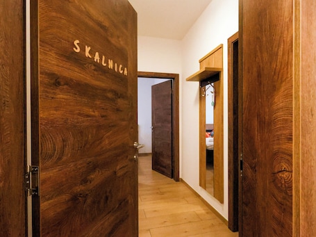 A wooden door with 'SKALNICA' carved on it, leading to a hallway with a wooden floor and a mirror on the wall.