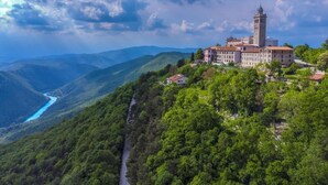 A historic building with a tower, surrounded by lush greenery and mountains.