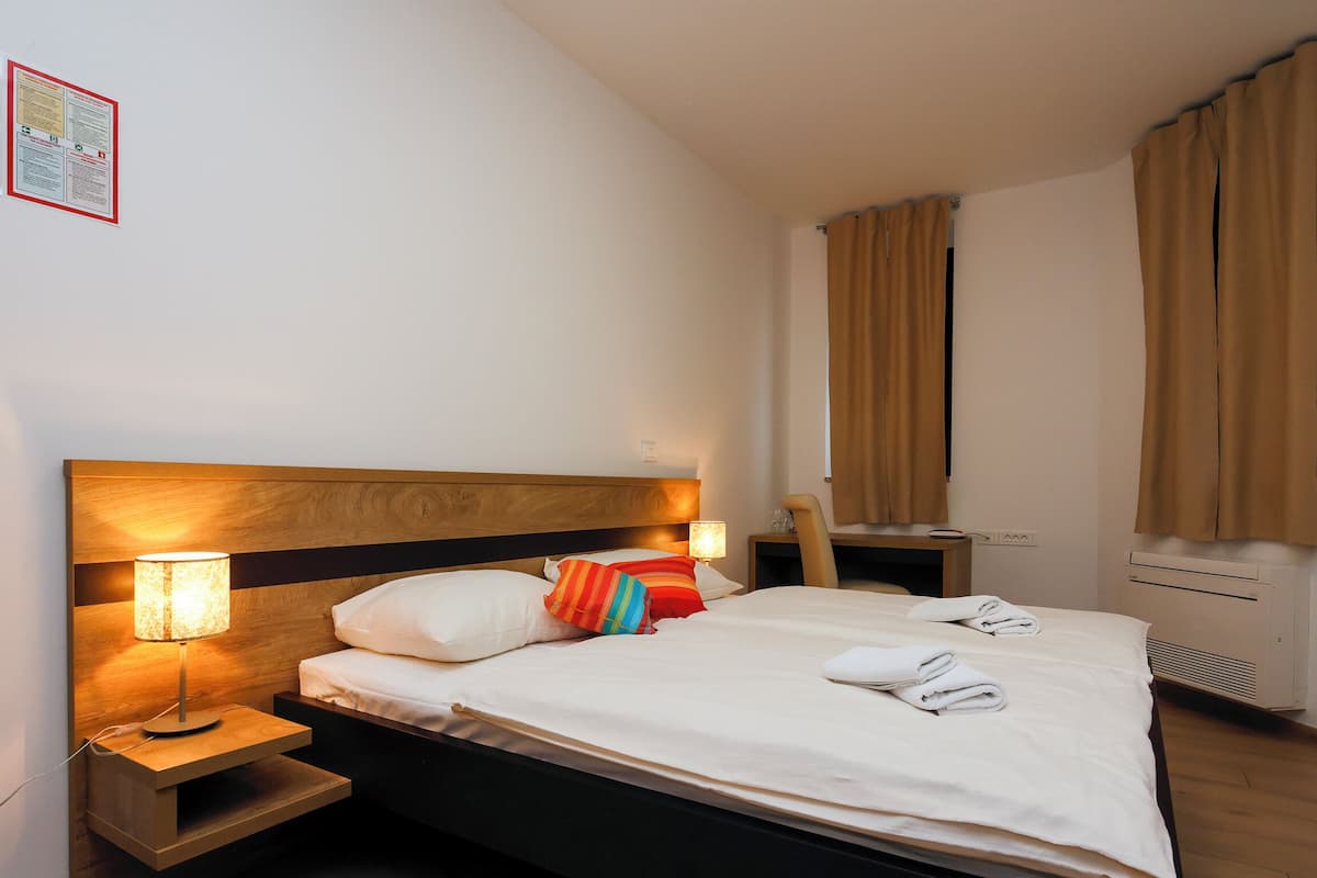 A hotel room with a bed, bedside lamps, a desk, and a window with curtains.