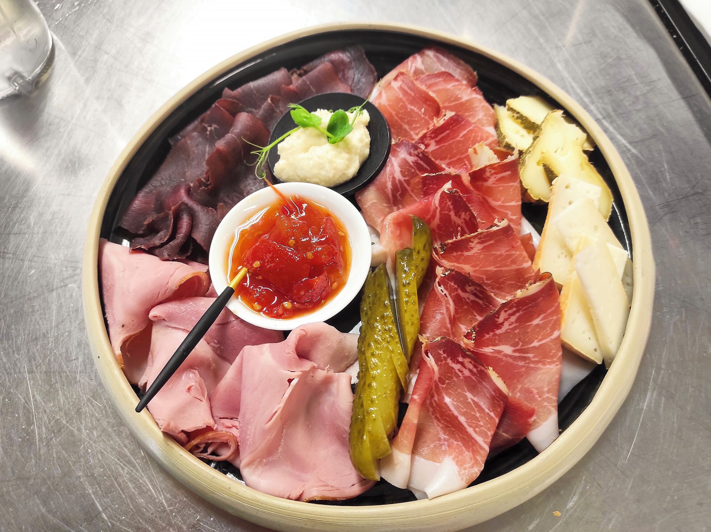 A plate of assorted meats, pickles, and a small bowl of sauce.