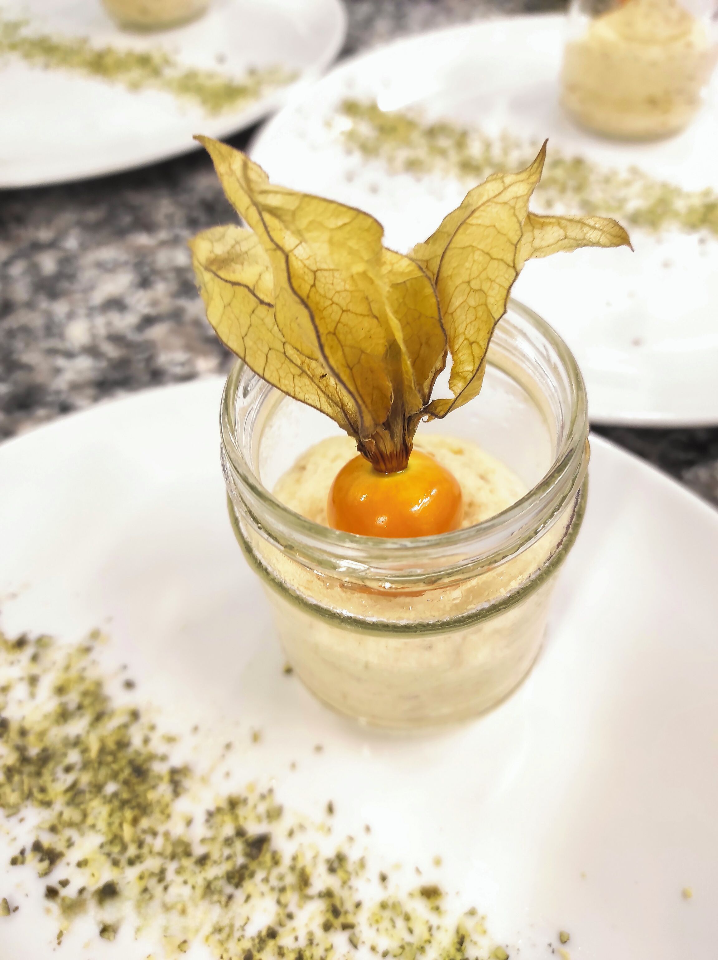 Un postre en un frasco con adorno de hoja sobre un plato blanco.