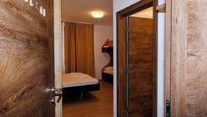 A wooden door with the word 'SOLK' partially visible, leading into a room with a bed, a small table, and a window with curtains.
