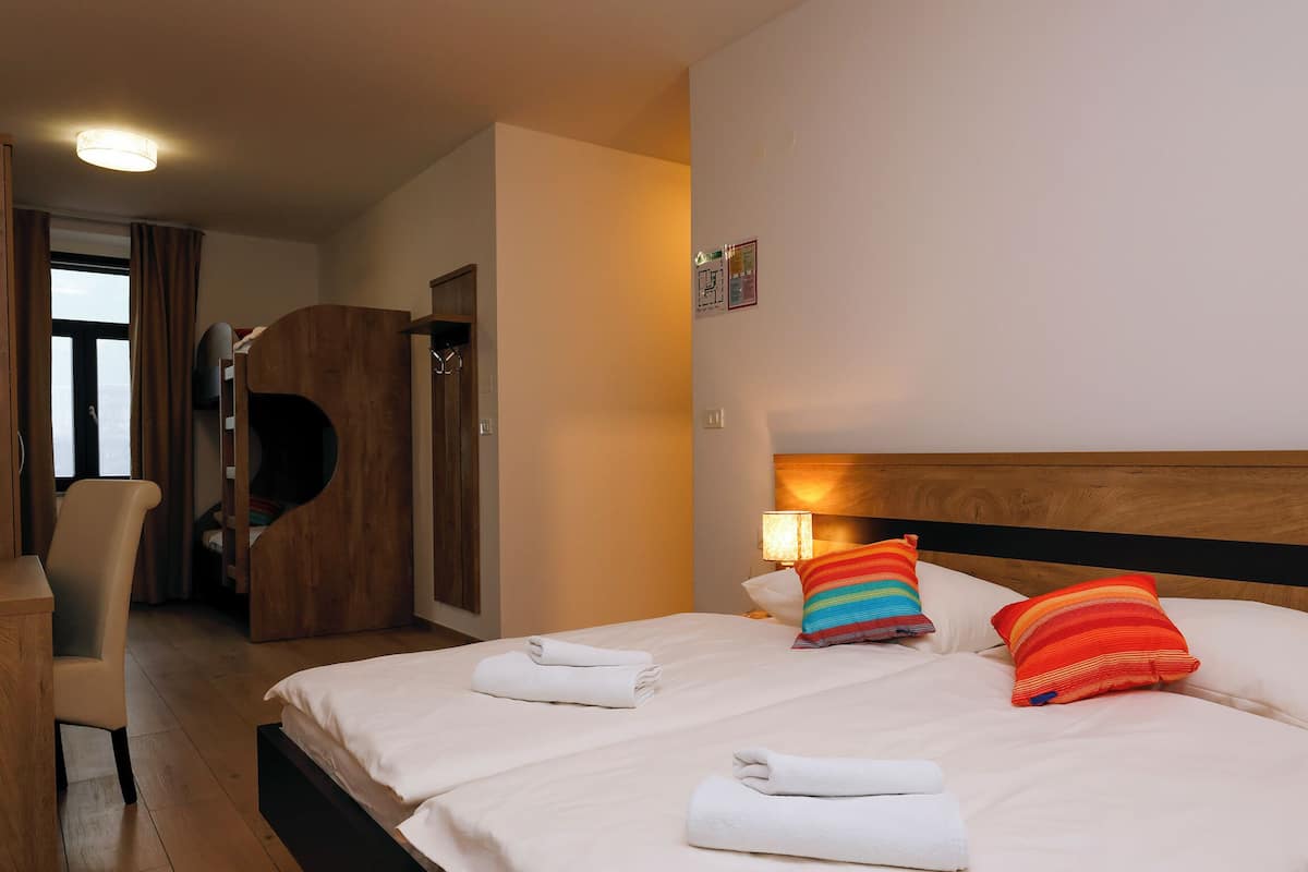 A hotel room with a bed, a chair, a wooden wardrobe, and a wall-mounted lamp.
