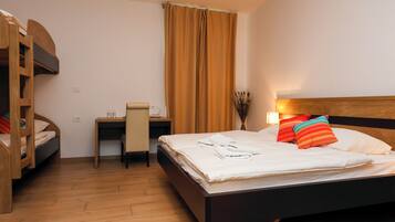 Ein Hotelzimmer mit Etagenbett, Schreibtisch mit Stuhl, Nachttisch, Lampe und einem Fenster mit Vorhängen.