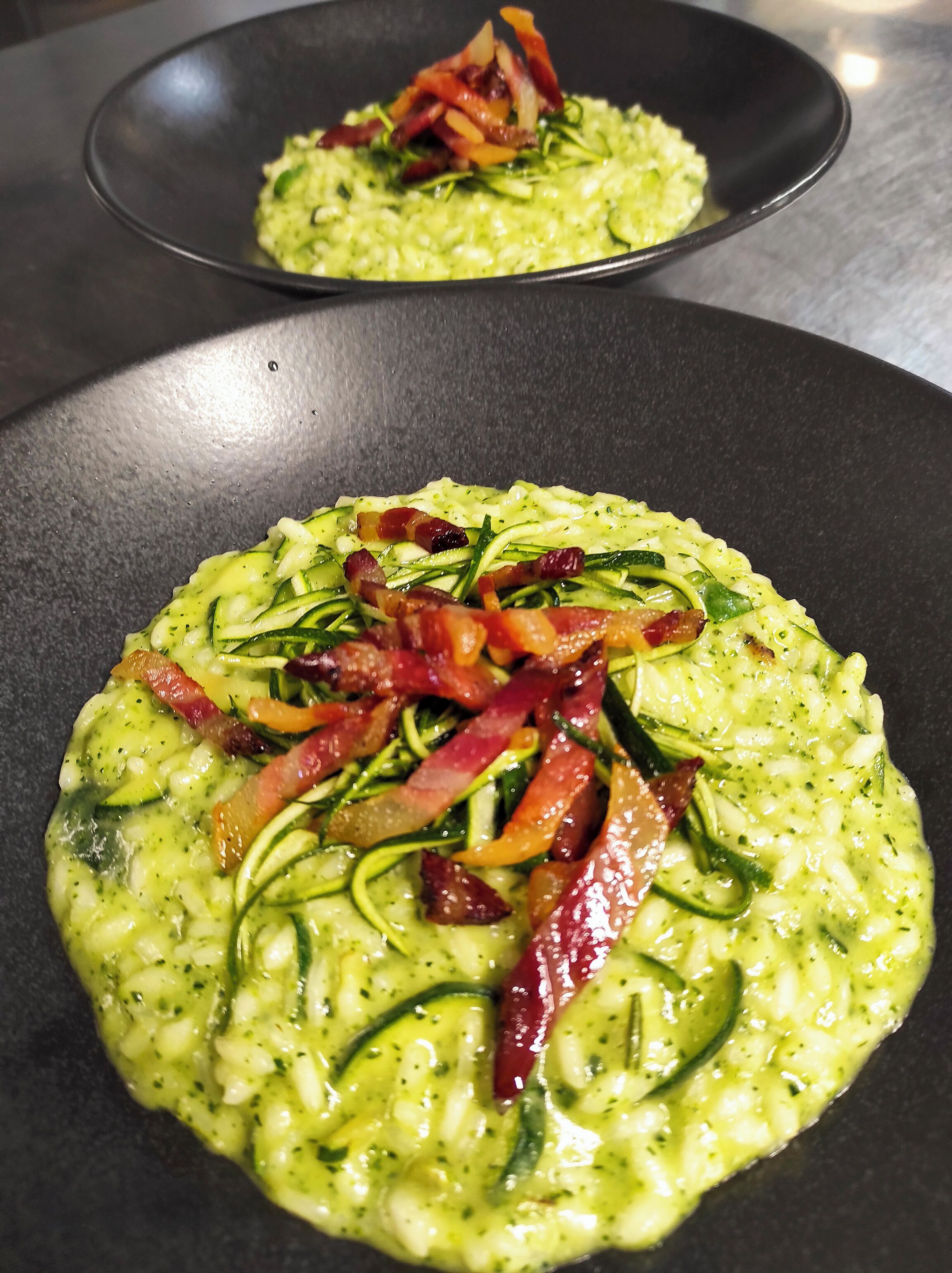 En rätt med zucchini och bacon, serverad på en svart tallrik.
