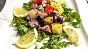 A white plate with a salad consisting of greens, potatoes, and lemon slices.