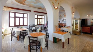 A restaurant with tables, chairs, a glass display case, and a ceiling mural.