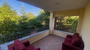 A balcony with two red sofas, a tiled floor, and a view of trees and a clear sky. - Room-cozy Rooms Near the Airport (Arnavutköy)