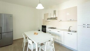 Une cuisine moderne avec des meubles blancs, un réfrigérateur en acier inoxydable, une cuisinière à gaz et une table à manger avec des chaises.