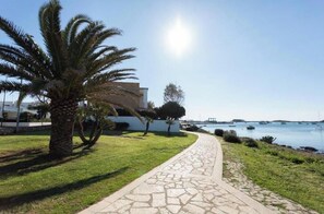 A paved pathway leading to a building with a palm tree and a view of the sea with boats. - Sole Holiday Home - Holiday home with terrace near the sea in Porto Cesareo (Porto Cesareo)