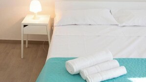 Un lit bien fait, avec du linge de lit blanc, une couvre-lit turquoise et des serviettes blanches pliées, posées sur le bord.