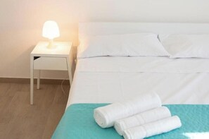 A neatly made bed with white linens, a teal bedspread, and rolled white towels on the side. - Sole Holiday Home - Holiday home with terrace near the sea in Porto Cesareo (Porto Cesareo)
