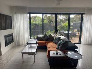 Ein modernes Wohnzimmer mit einer Couch, einem Couchtisch und Blick auf einen Garten durch große Glasfenster.