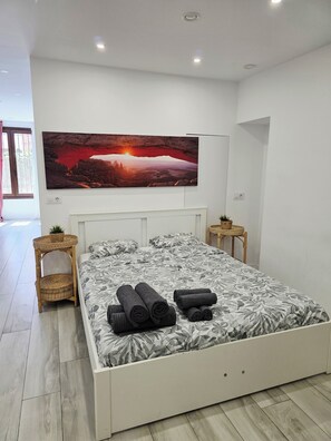 Ein modernes Schlafzimmer mit einem großen Bett, einem Wand-Fernseher, einem kleinen Nachttisch und einem Korbstuhl.