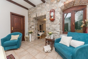 A cozy room with a stone wall, a wooden door, a clock, a blue sofa, and a small table with a vase. - Apartman Listun (Makarska)