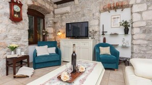 Ein Zimmer mit steinwänden, einem Fernseher, zwei blauen Sofas, einem Holztisch mit Tablett und einer Uhr.