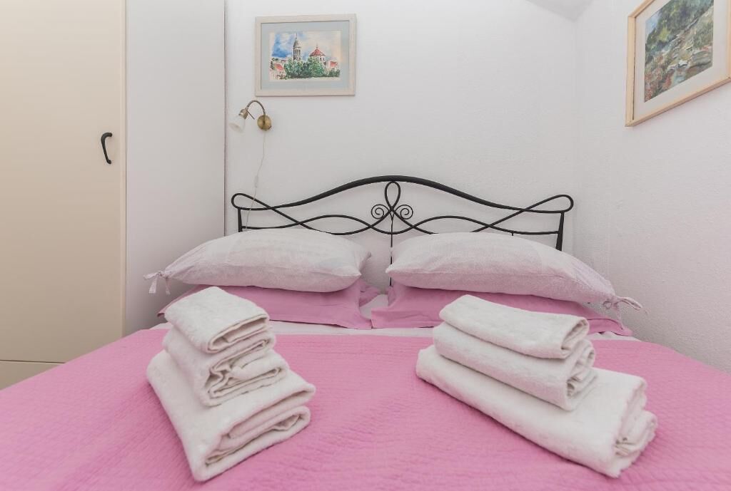 Un letto con biancheria rosa, due cuscini e asciugamani piegati.