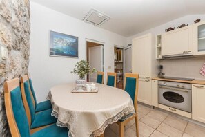 A small dining area with a table, chairs, and a view of the kitchen. - Apartman Listun (Makarska)