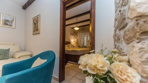 Ein Zimmer mit einem Bett, einem blauen Sessel, einer Couch, einem Wandbild und einer Vase mit Blumen.