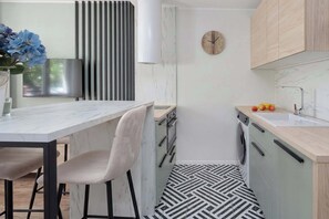 Uma cozinha moderna com bancada de mármore, pia, relógio e máquina de lavar.