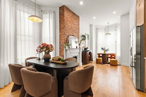 A dining area with a brick wall, a fireplace, and a modern kitchen with a refrigerator.