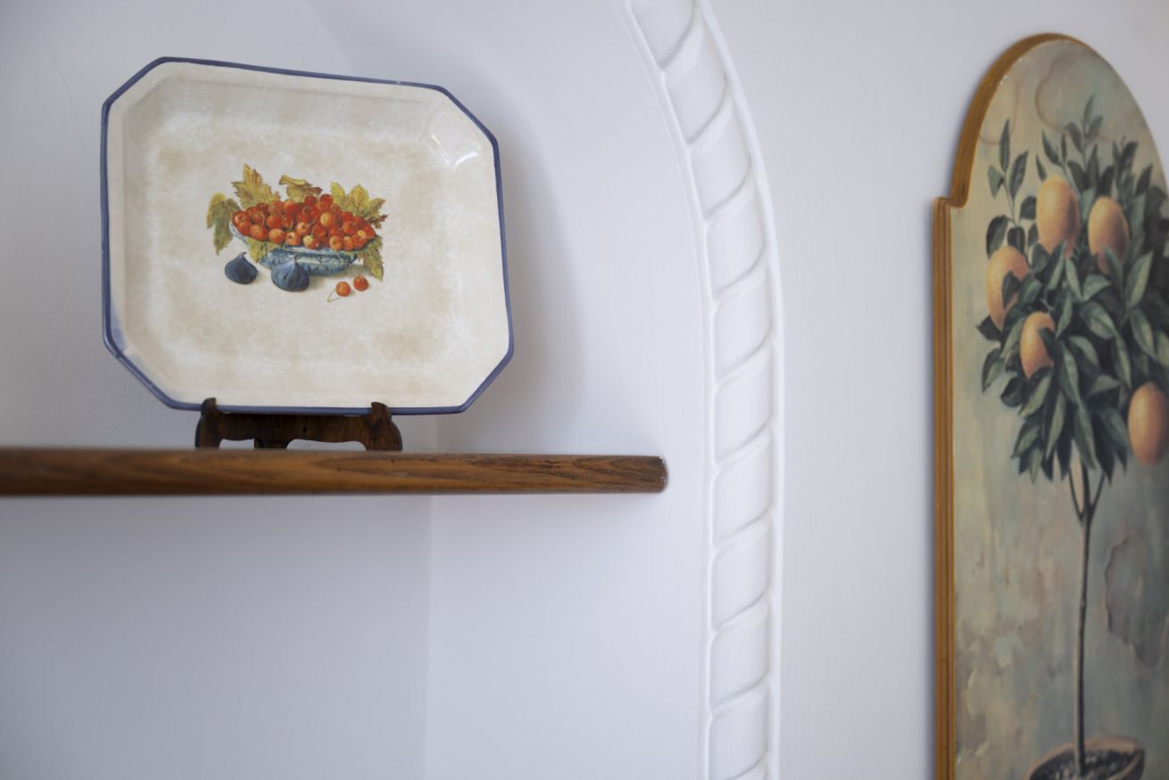 A ceramic plate with a fruit design, a wooden shelf, and a wall with a textured pattern.