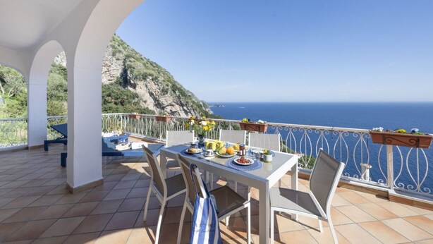 Una terraza con una mesa lista para comer, con vista a un paisaje costero.