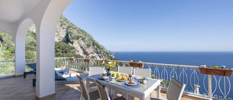 Una terraza con una mesa lista para comer, con vista a un paisaje costero.
