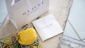 Una bolsa de papel blanca y una tarjeta blanca con el texto 'MAREME' sobre una superficie de madera.