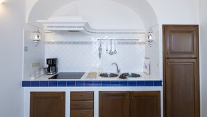 Una cocina con salpicadero de azulejos blancos, un lavamanos de acero inoxidable, armarios de madera y un horno empotrado.