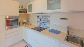 Ett modernt kök med vita skåp, en ugn i rostfritt stål, en kaffebryggare och en väggdekoration med fiskmotiv.