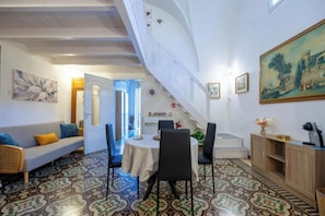 Une pièce comprenant une table à manger, des chaises, un canapé, un escalier et un tableau accroché au mur.