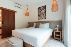 Een hotelkamer met een bed, bedlampen, een airconditioningsunit en een groot raam met gordijnen.