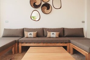 Een modulaire bank met twee kussens, een houten salontafel en wandplanken van geweven manden.