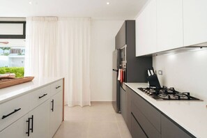 Een moderne keuken met een gasfornuis, een koelkast en een raam met gordijnen.