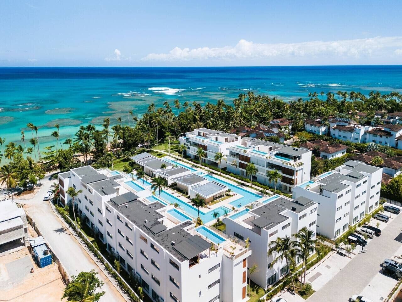 Un complejo turístico con varias edificaciones, un área de piscina y vista al océano.