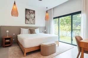 Ein modernes Schlafzimmer mit einem großen Bett, Nachttischlampen, einem kleinen Tisch und Blick auf Grün durch große Fenster.