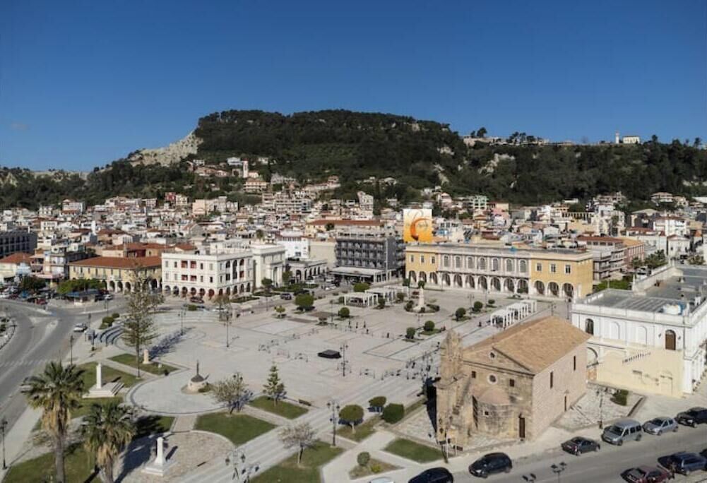 Un paisaje urbano con una plaza destacada, edificios históricos y una colina al fondo.