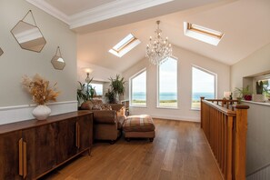 Ein geräumiges Wohnzimmer mit Holzboden, einer großen Kronleuchter und Meerblick durch große Fenster.