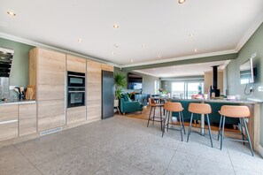 Eine moderne Küche mit eingebauten Geräten, ein Essbereich mit Barhocker und ein Wohnbereich mit Sofa und Fernseher.