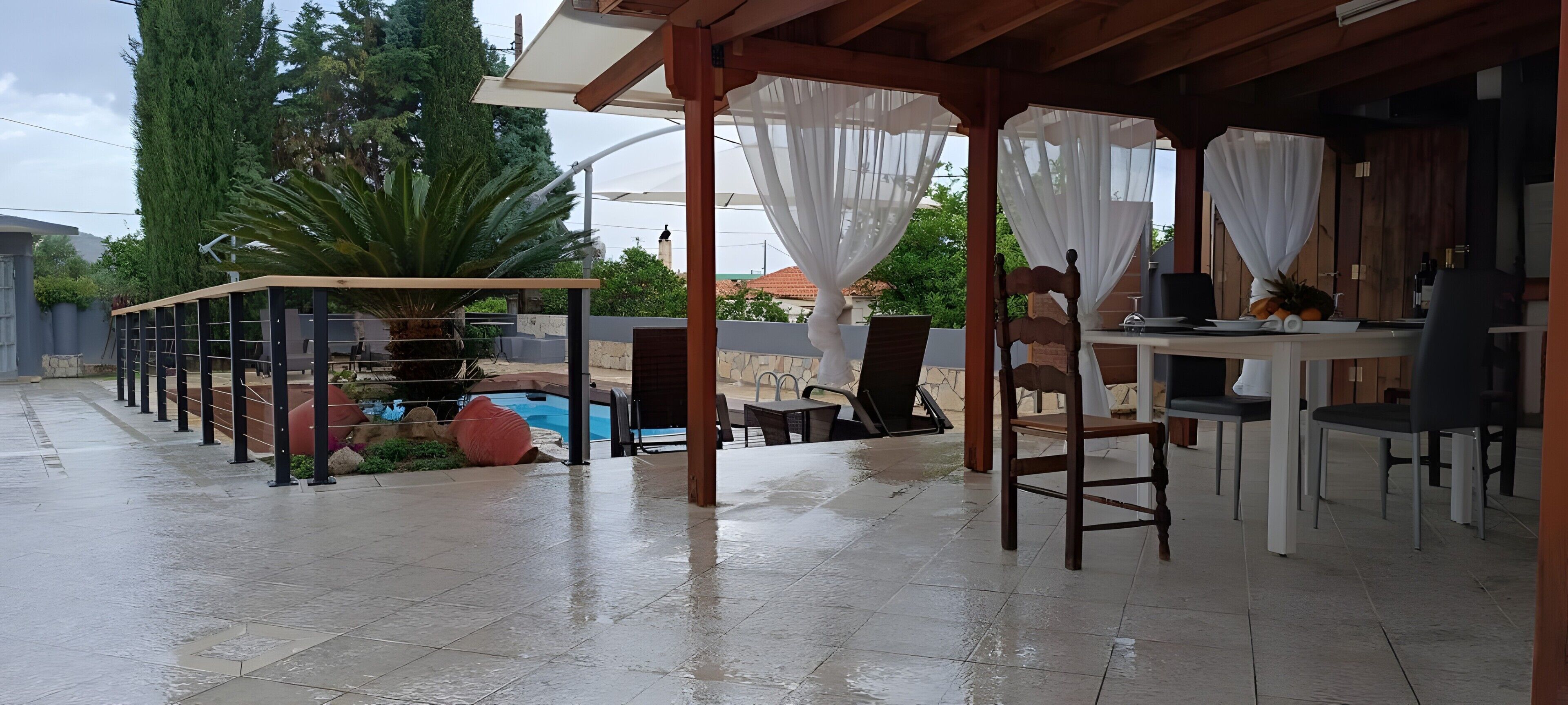 Un área de patio exterior con piscina, mobiliario cubierto y una mesa con sillas.